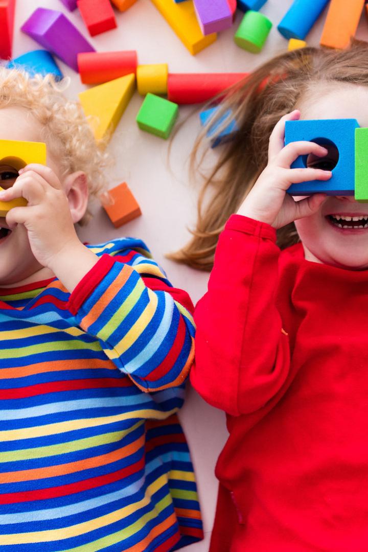 Zwei Kinder spielen mit bunten Bauklötzen und halten sie vor ihre Augen.