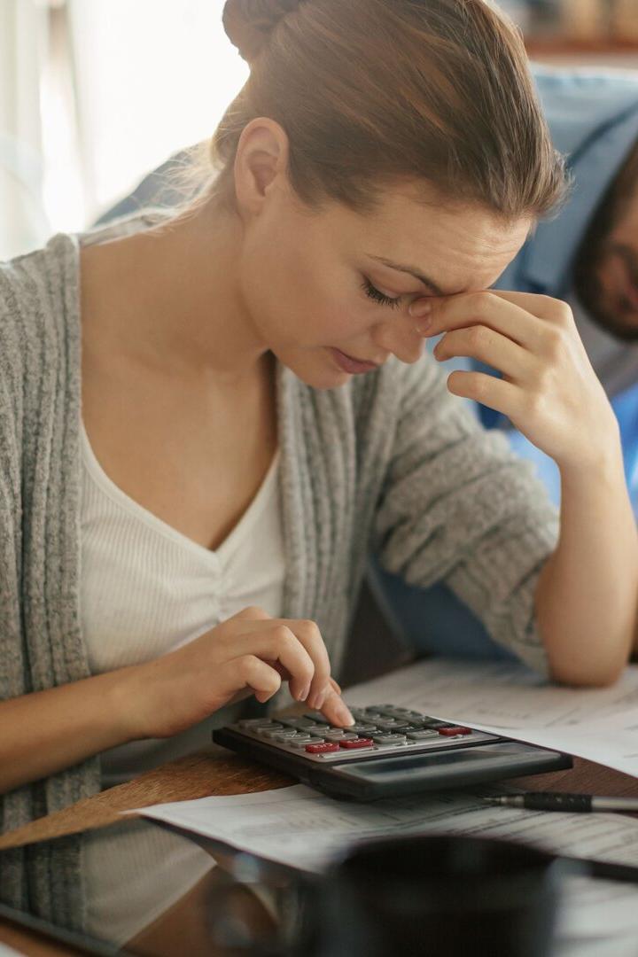 Ein besorgtes Paar sitzt mit Rechnungen und einem Taschenrechner am Tisch.