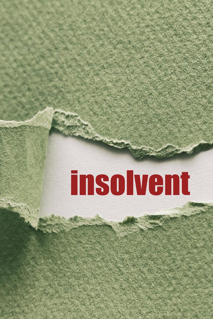 Das Wort „insolvent“ ist durch ein Loch in einem grünen Blatt Papier sichtbar.