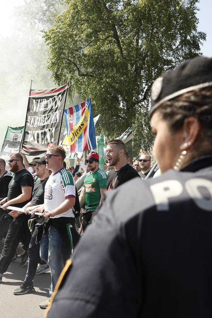 Eine Polizistin steht vor einer Gruppe Fußballfans mit Fahnen und Rauch.