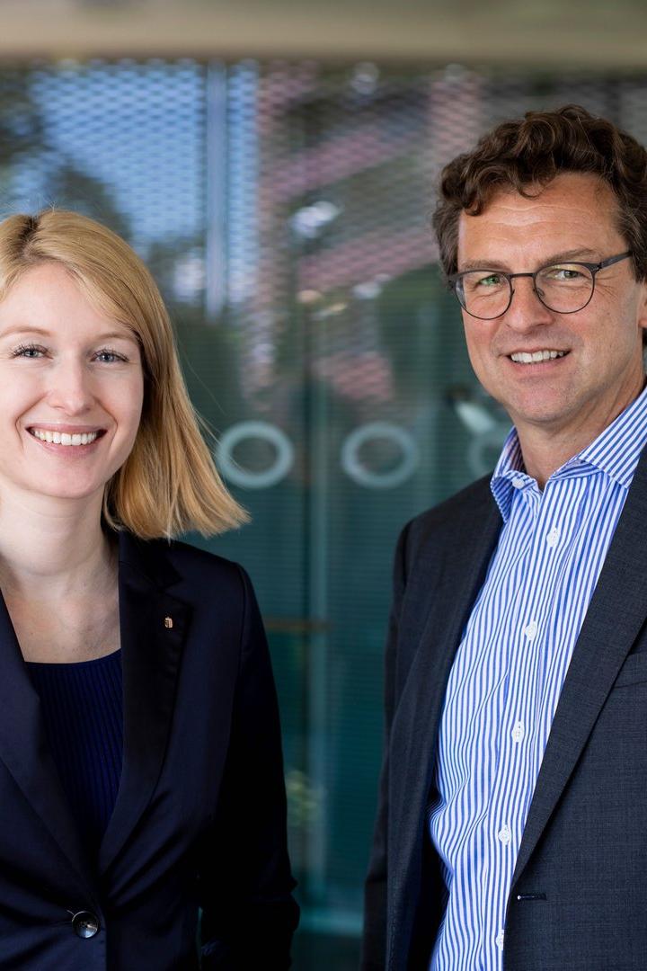 Eine blonde Frau und ein Mann mit Brille lächeln in die Kamera.