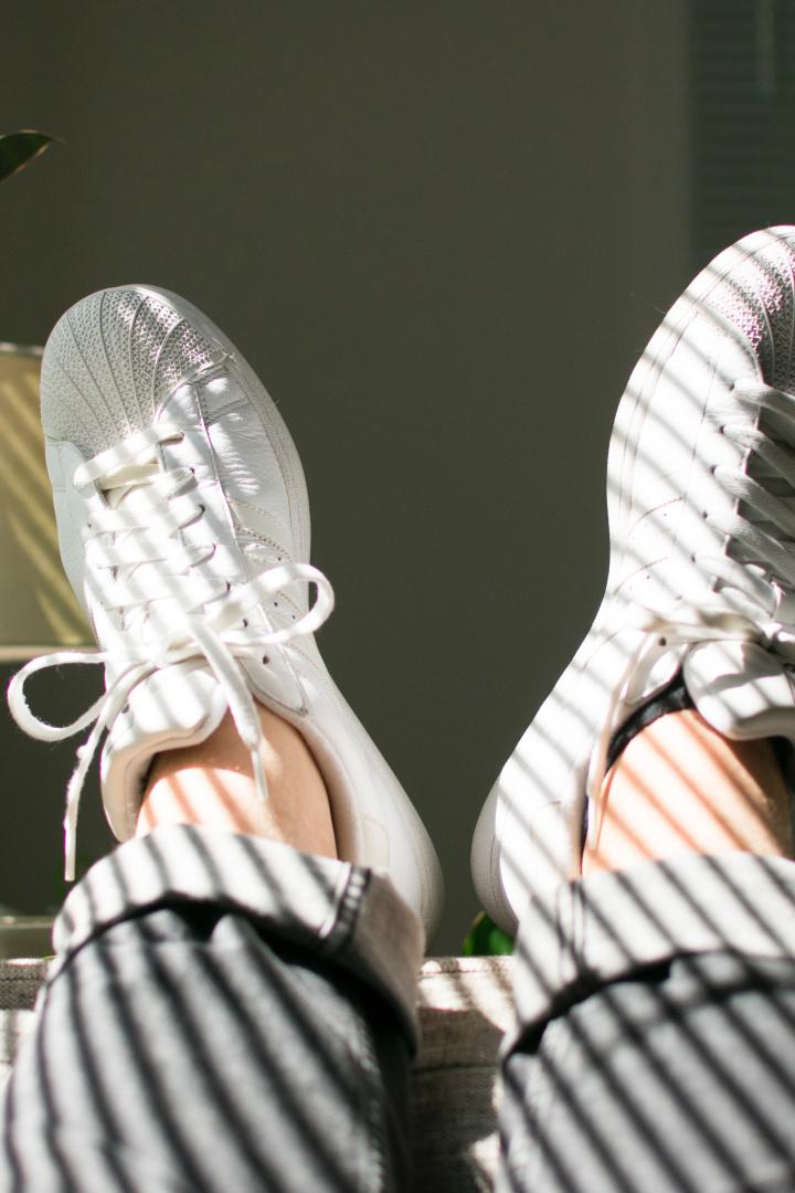 Beine mit weißen Turnschuhen liegen auf einem Sofa im Sonnenlicht.