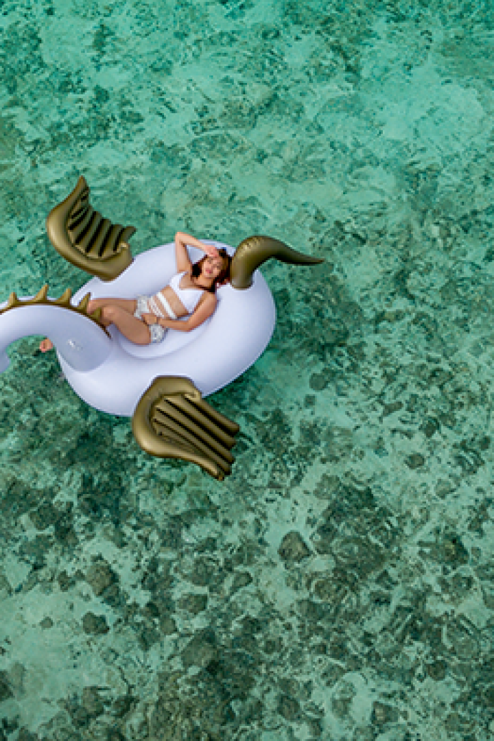 Eine Frau entspannt auf einer aufblasbaren Drachenliege im türkisfarbenen Wasser.