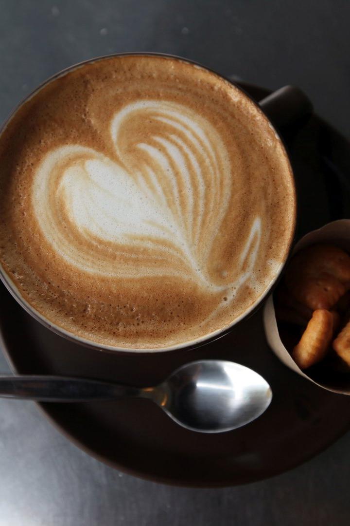 Ein Cappuccino mit Herzmuster im Milchschaum, serviert mit einer kleinen Portion Gebäck.