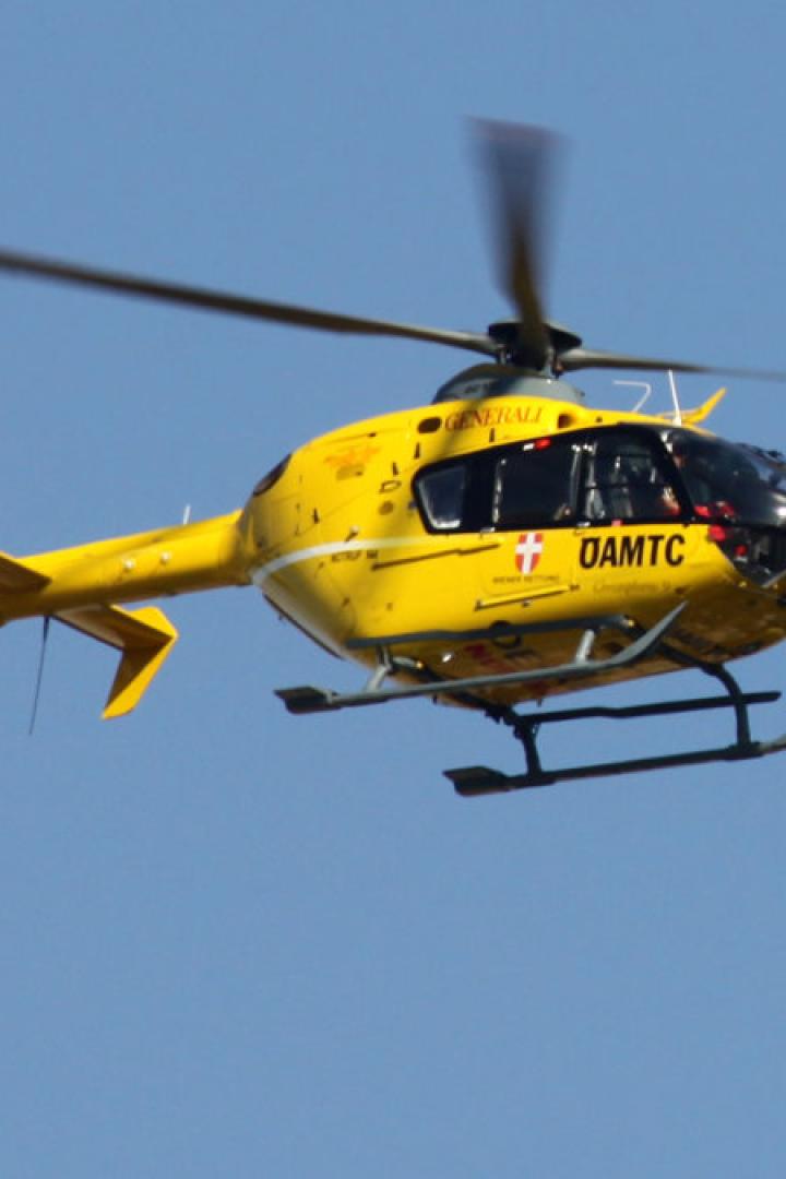 Ein gelber Rettungshubschrauber des ÖAMTC fliegt vor blauem Himmel.