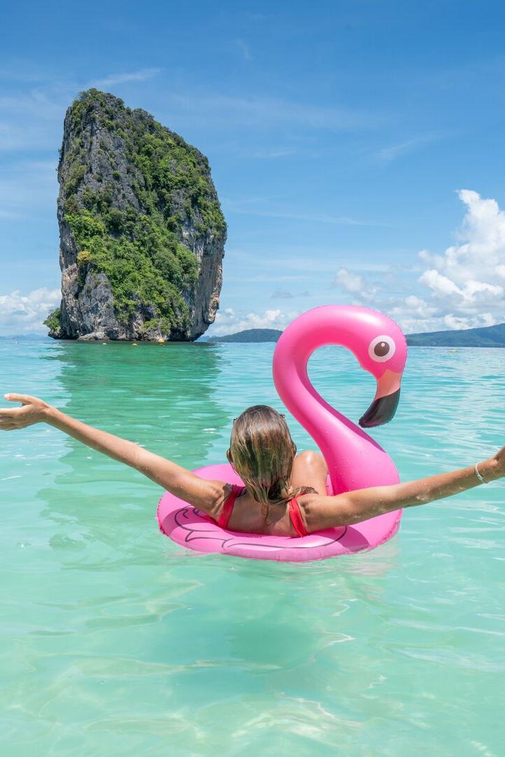 Frau im Meer in Thailand auf einem pinken, aufblasbaren Plastik-Flamingo, Sonnenschein und Urlaub