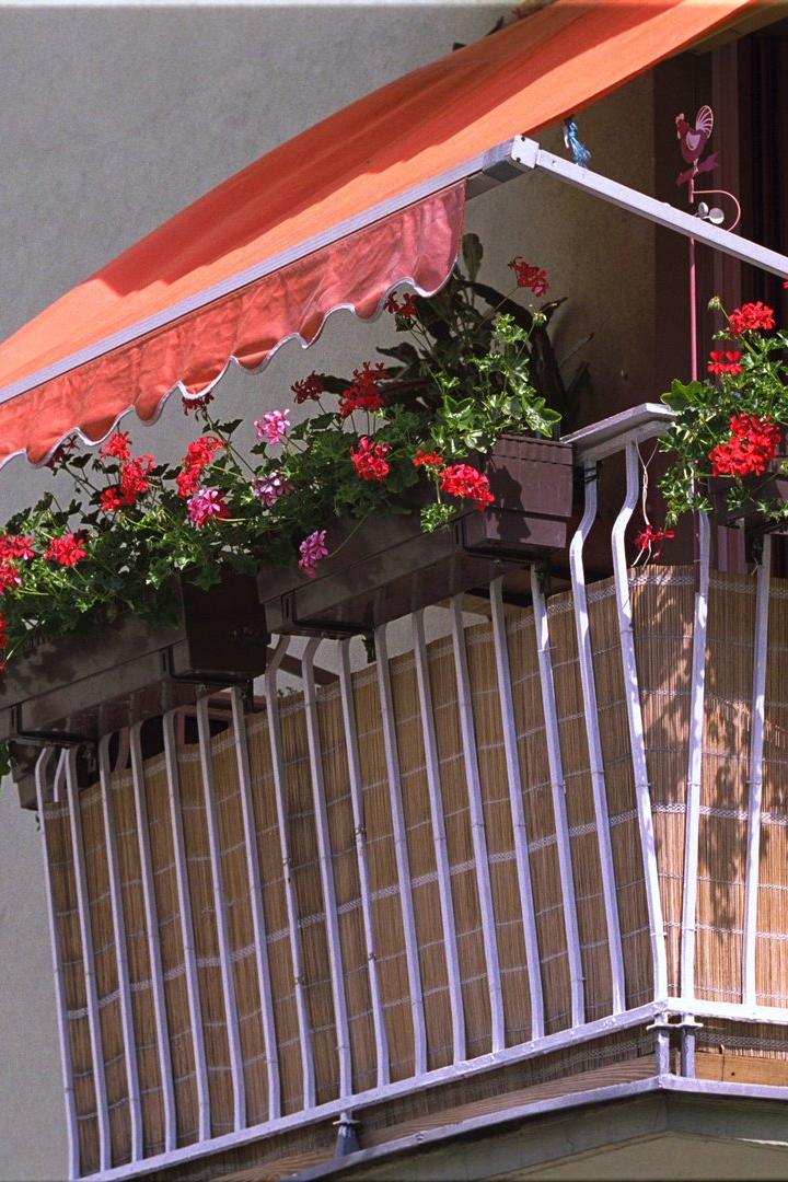 Ein Balkon mit roter Markise und üppigen Geranienkästen.