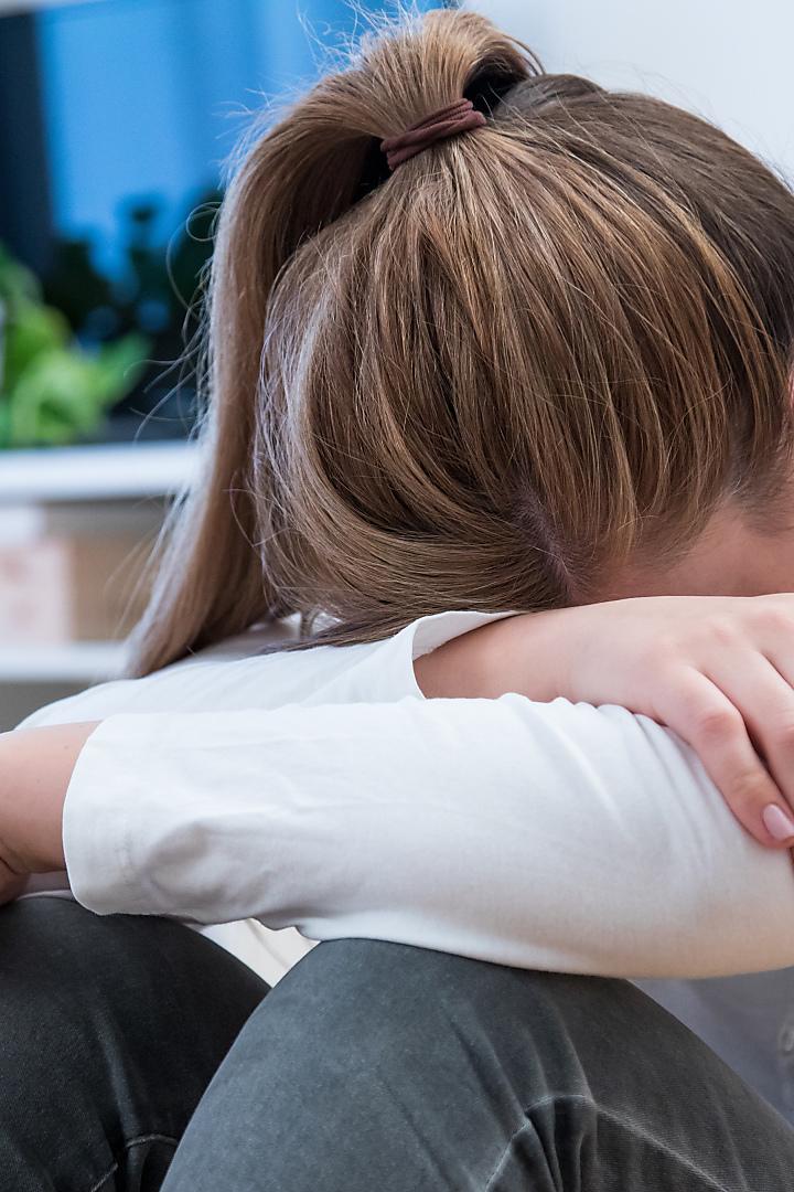 Eine Frau sitzt mit gesenktem Kopf und verschränkten Armen auf dem Boden.