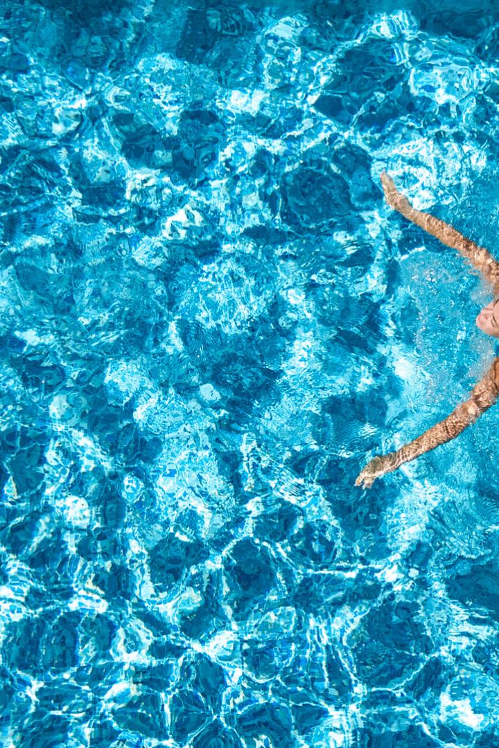 Aerial drone view of active girl in swimming pool from above, yong woman swims in blue water, tropical vacation, holiday on resort concept