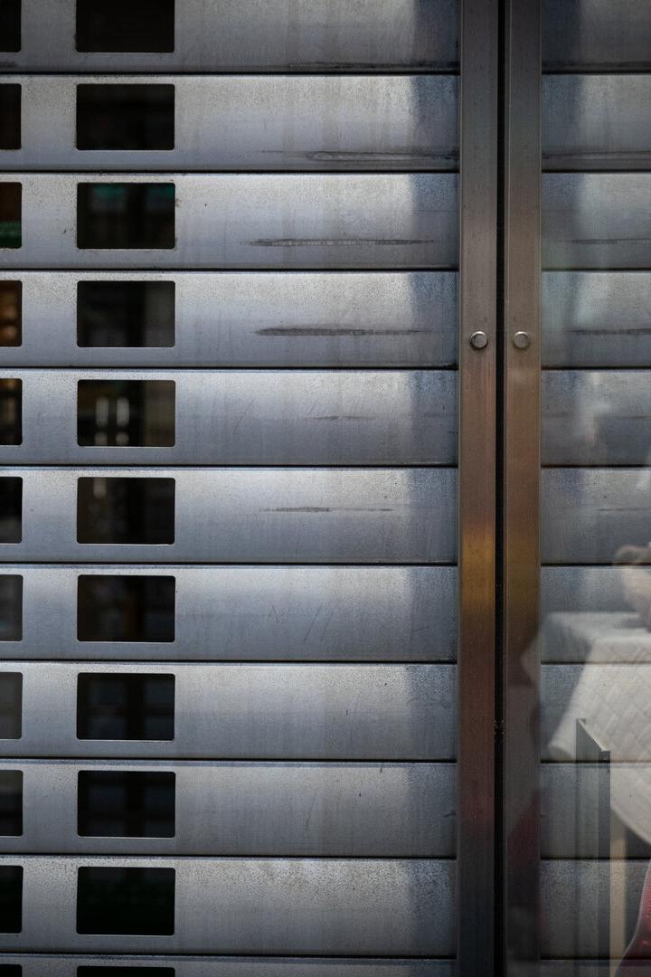 Zwei Schaufensterpuppen mit Winterkleidung stehen hinter einem teilweise geschlossenen Metallrolltor.