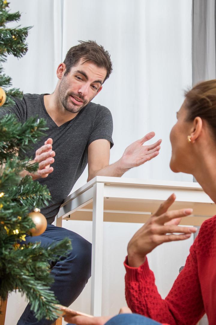 Pärchen sitzt neben Christbaum und streitet sich.