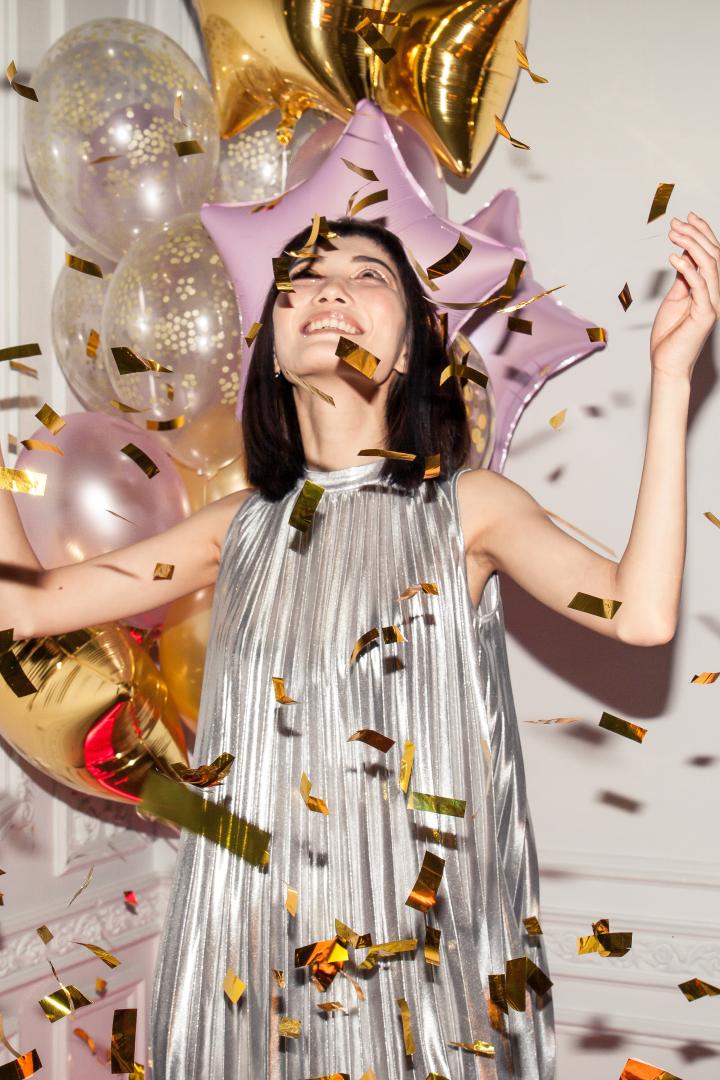 Frau steht im silbernen Kleid im Konfetti-Regen.