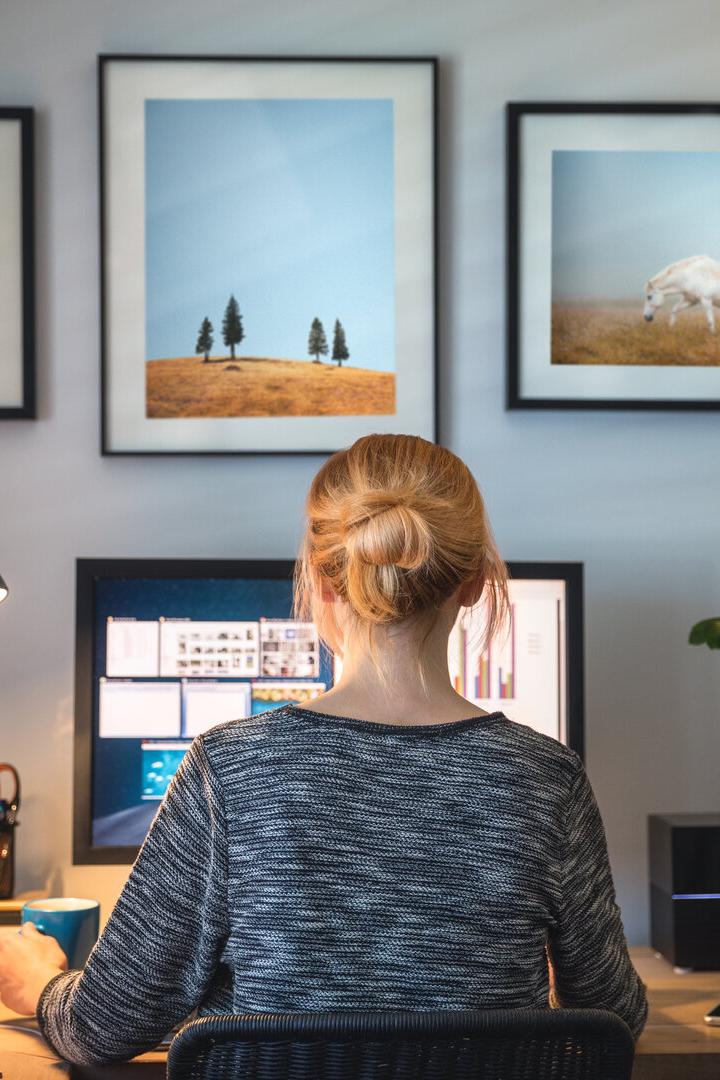 Eine Frau sitzt vor einem Computer an einem Schreibtisch mit drei Bildern an der Wand.