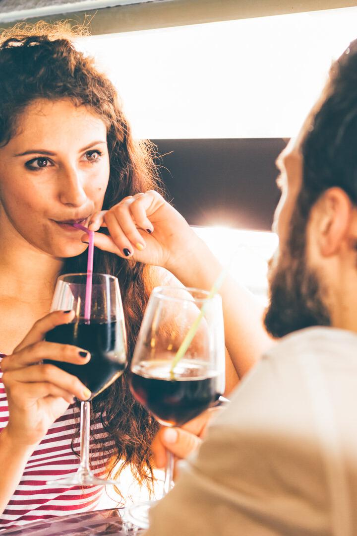 Eine Frau mit lockigem Haar und ein bärtiger Mann sitzen sich gegenüber und trinken ein Getränk aus Gläsern mit Strohhalmen.