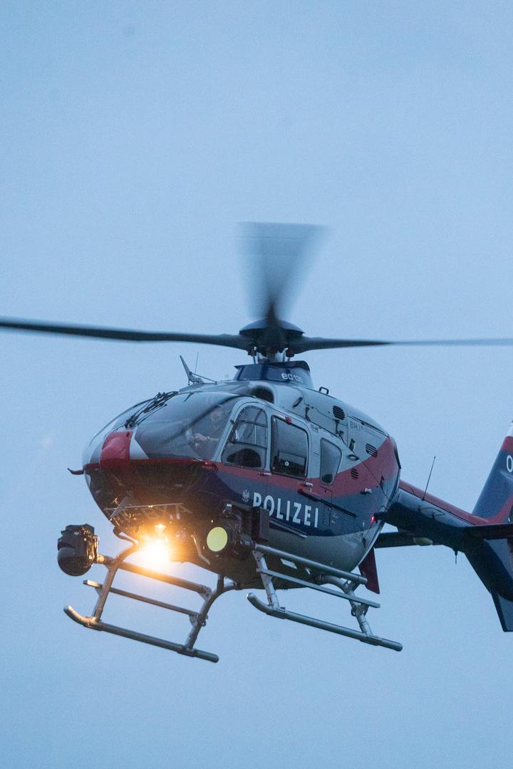Ein rot-blau-weisser Polizei-Hubschrauber mit der Kennung OE-BXA ist in der Luft.