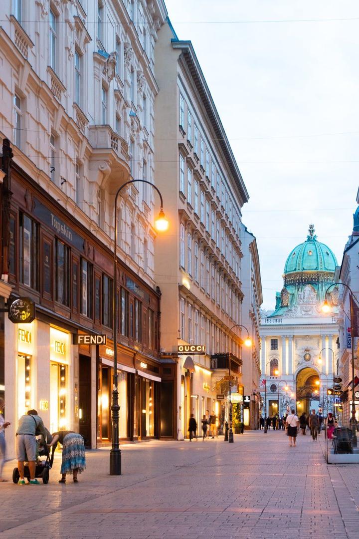Blick auf eine belebte Einkaufsstraße in Wien mit Geschäften wie Armani, Fendi und Gucci.