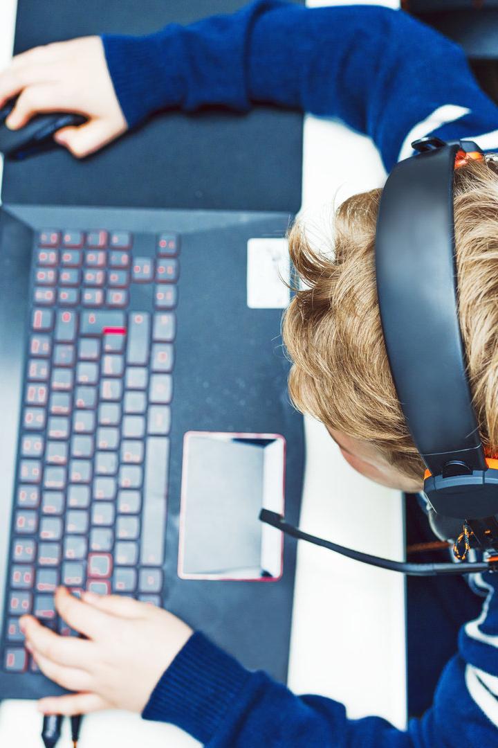 Ein Kind spielt mit einem Headset ein Computerspiel auf einem Laptop.