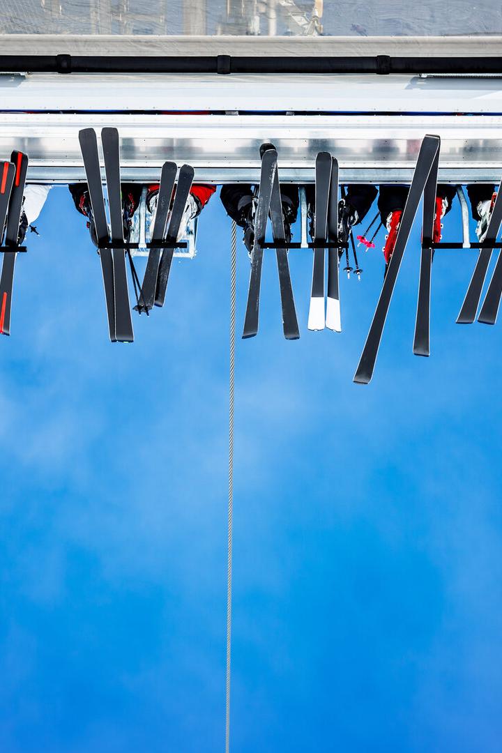 Menschen auf einem Sessellift von unten, Ski vor blauem Himmel