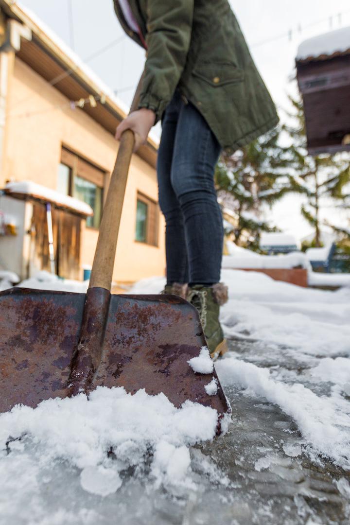 Eine Person schaufelt Schnee  vor einem Haus.
