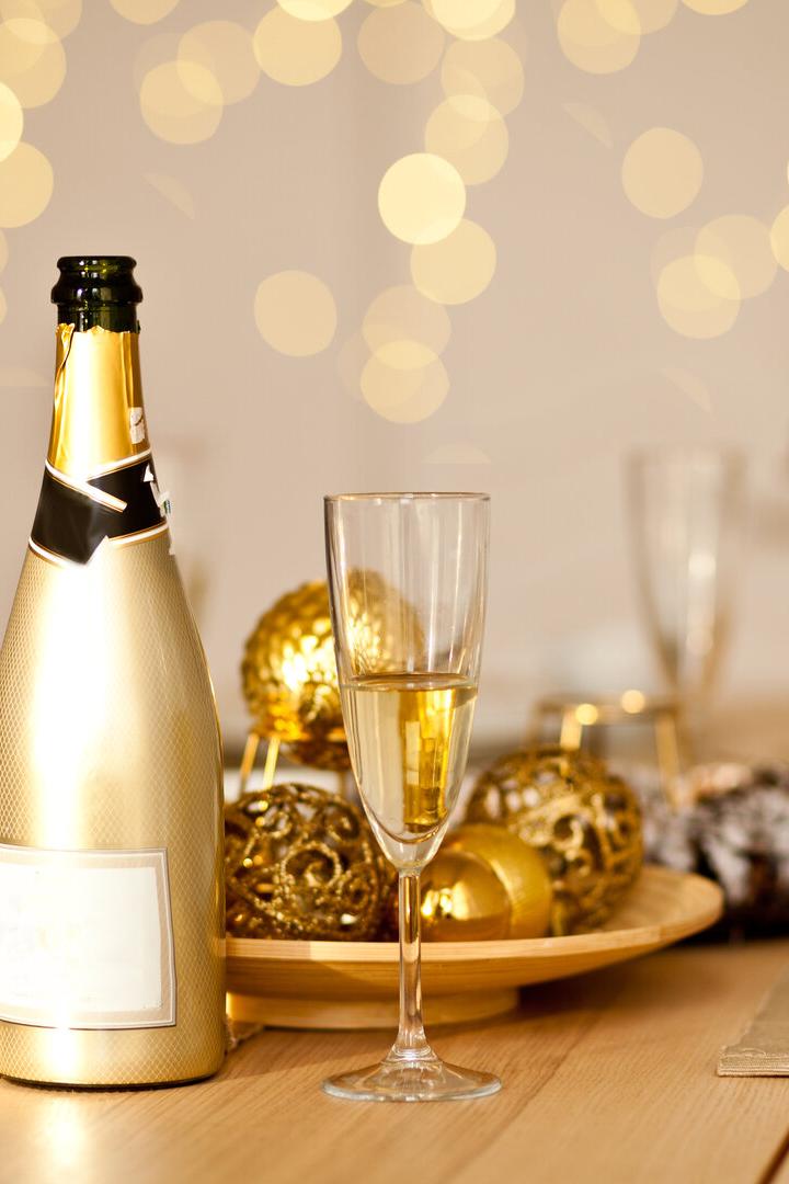Eine goldene Sektflasche und ein gefülltes Glas stehen auf einem festlich gedeckten Tisch mit goldener Dekoration.