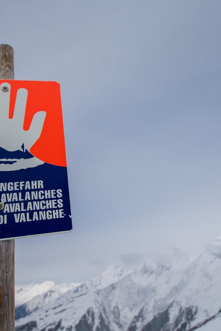 Ein Lawinengefahr-Schild steht vor einer verschneiten Berglandschaft.