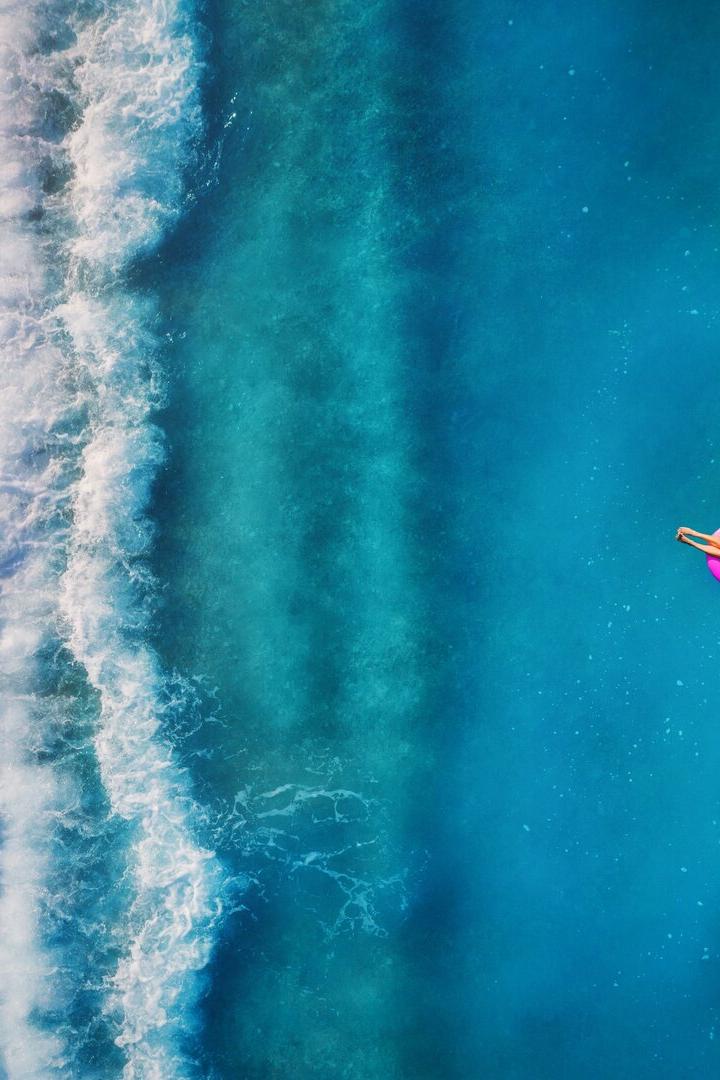 Aerial view of young woman swimming on the pink swim ring in the transparent turquoise sea in Oludeniz. Summer seascape with girl, beach, beautiful waves, blue water at sunset. Top view from drone