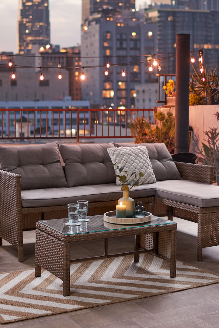 Eine Lounge-Ecke mit Sofa und Tisch auf einer Dachterrasse mit Blick auf die Stadt bei Nacht.