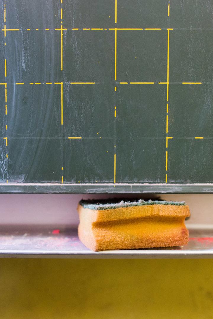 Ein Schwamm liegt auf der Ablage vor einer grünen Tafel mit gelbem Raster.