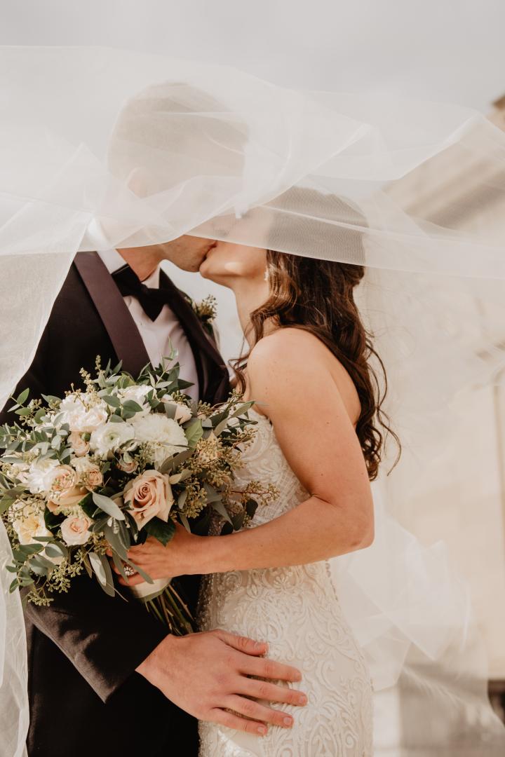 Brautpaar küsst sich unter einem weißen Schleier.