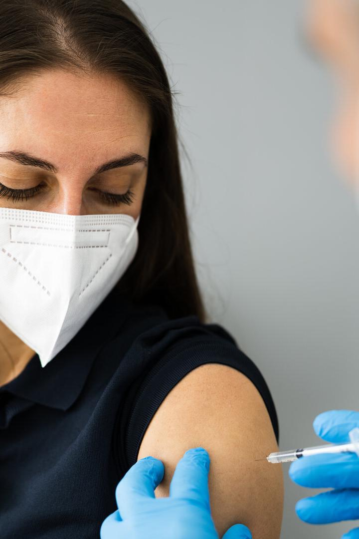 Eine Frau mit Maske erhält eine Impfung in den Oberarm von einem Arzt mit Handschuhen.