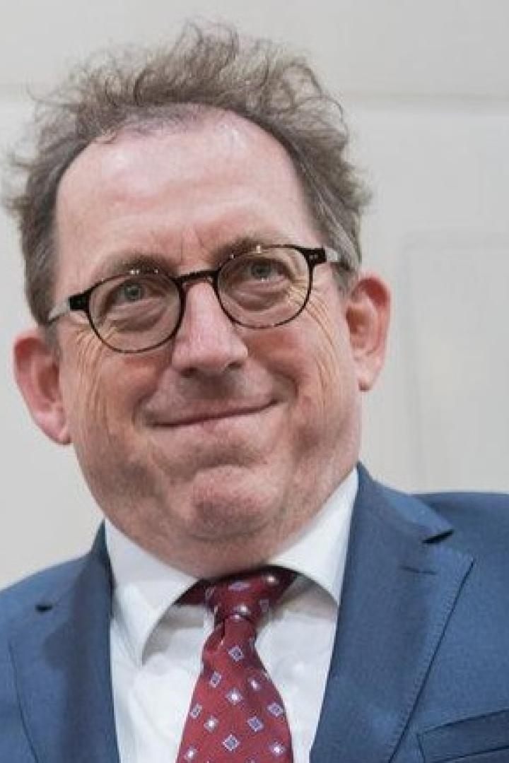 Ein älterer Mann hält eine rote Mappe des Presseclub Concordia und einen Blumenstrauß, flankiert von zwei Männern.