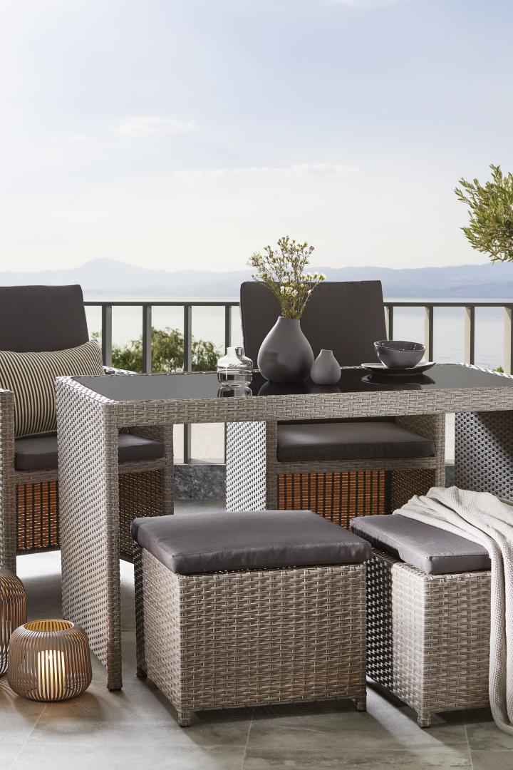 Ein Gartentisch mit Stühlen und Hockern auf einer Terrasse mit Meerblick.