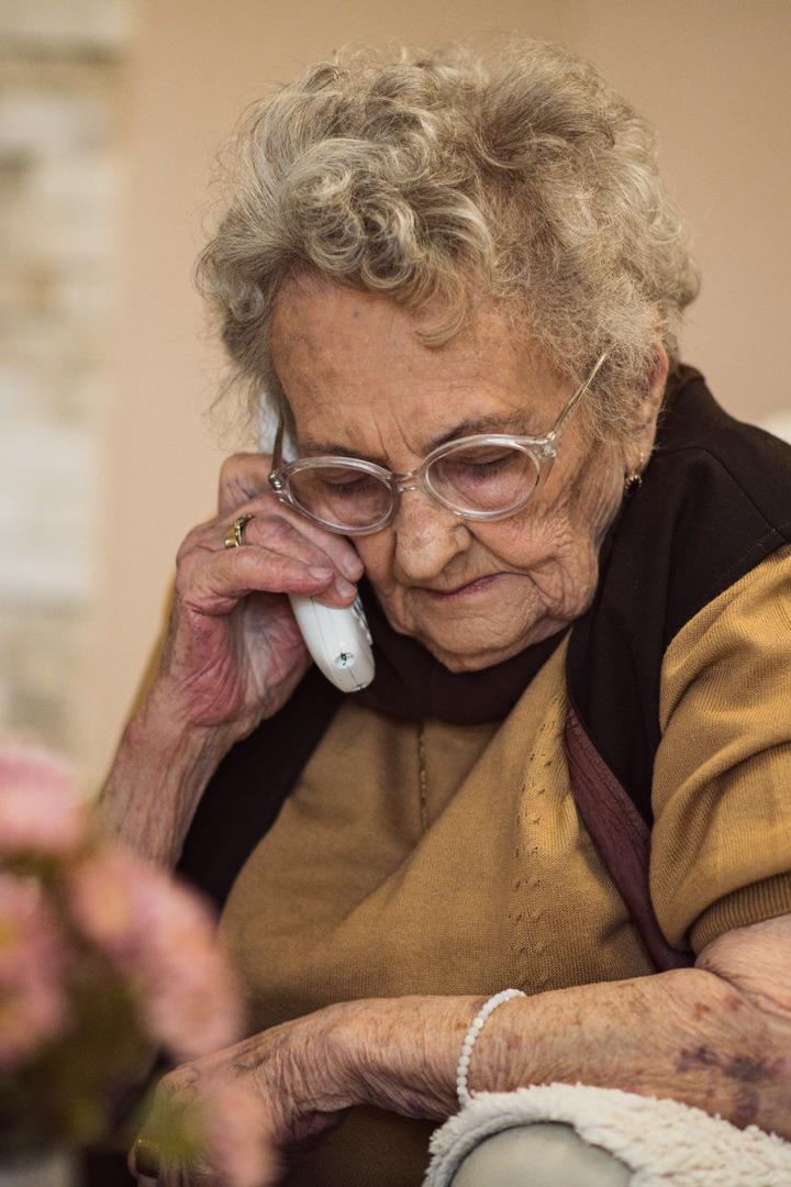 Eine ältere Frau mit Brille telefoniert mit einem weißen Telefon.