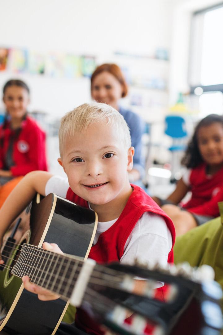 Ein Junge mit Down-Syndrom spielt Gitarre und lächelt, während andere Kinder um ihn herum auf Sitzsäcken sitzen.