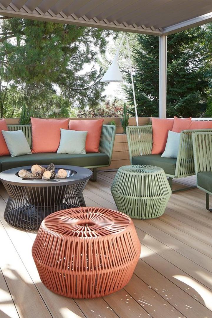 Eine Terrasse mit grünen Sofas, korallenroten Kissen und geflochtenen Hockern.
