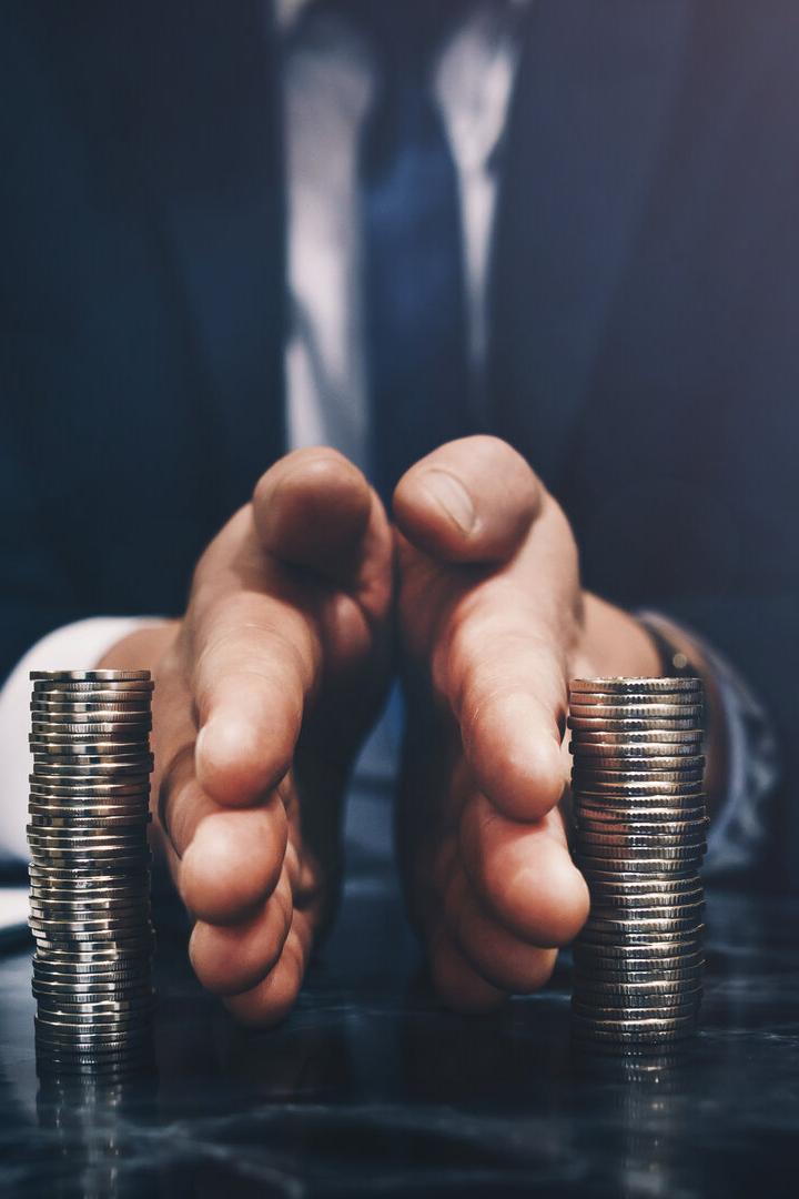 Ein Mann im Anzug trennt mit den Händen zwei Stapel Münzen auf einem Tisch voneinander.