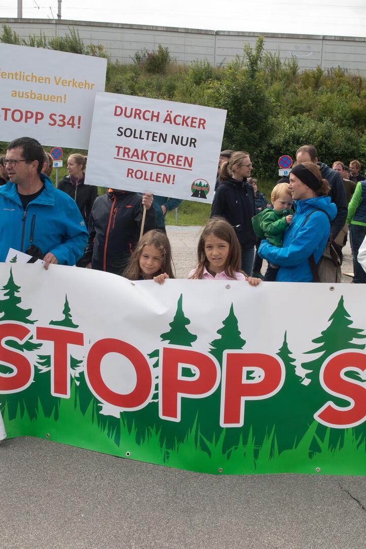 Demonstrierende mit Protestplakaten gegen die S34 und für den Ausbau des öffentlichen Verkehrs, einige Kinder vorn.