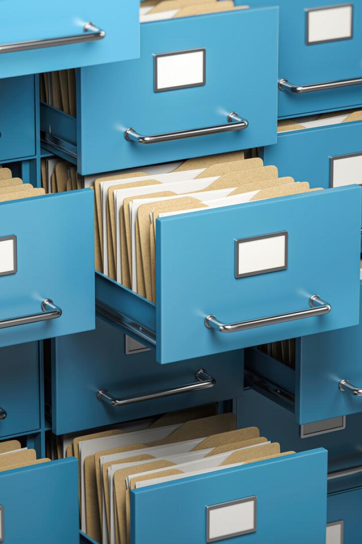Mehrere geöffnete blaue Aktenschubladen mit zahlreichen sortierten Aktenordnern und leeren Beschriftungsfeldern.