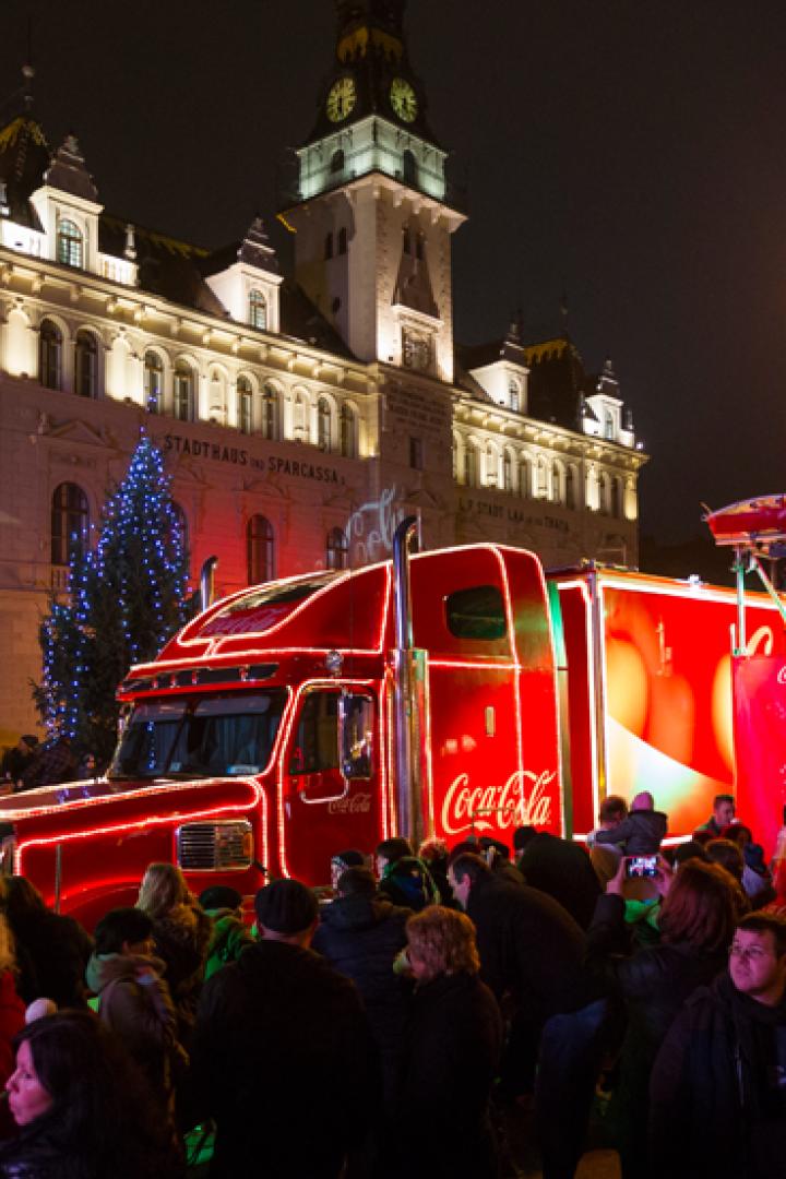 Ein beleuchteter Coca-Cola-Truck steht vor dem Rathaus auf einem belebten Platz.