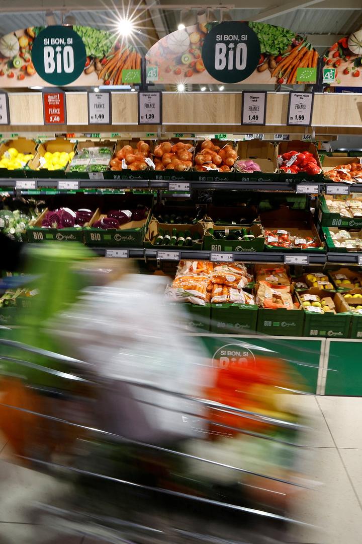 Ein Kunde schiebt einen Einkaufswagen durch die Gemüseabteilung eines Supermarktes.