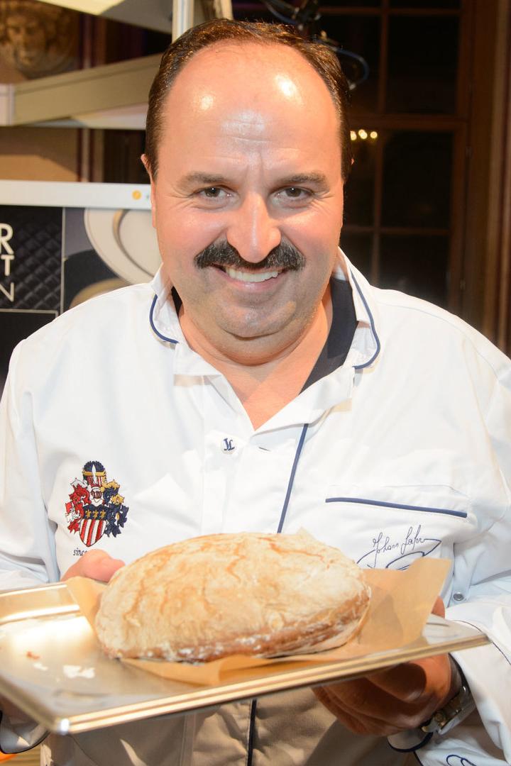 Ein lächelnder Koch präsentiert ein frisch gebackenes Brot auf einem Tablett.