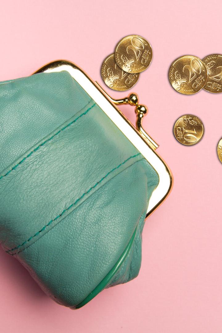 Ein türkisfarbenes Portemonnaie liegt auf rosa Untergrund, daneben mehrere goldene Münzen.