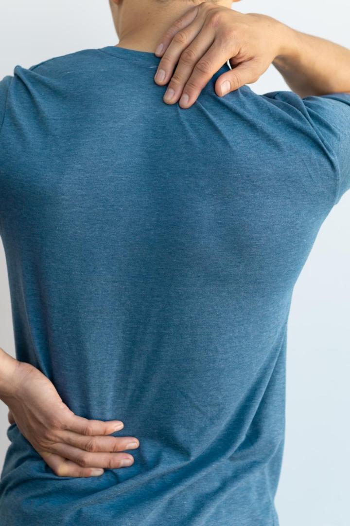 Ein Mann in einem blauen T-Shirt hält sich den Rücken und die Schulter, möglicherweise aufgrund von Schmerzen.