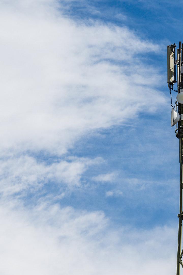 Ein Mobilfunkmast steht vor einem blau-weissen Himmel.