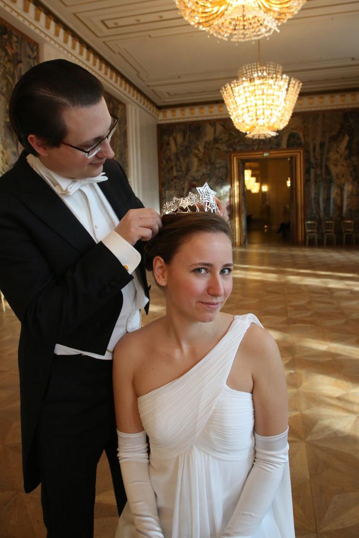 Ein Mann im Smoking setzt einer Frau im weißen Kleid eine Tiara auf.