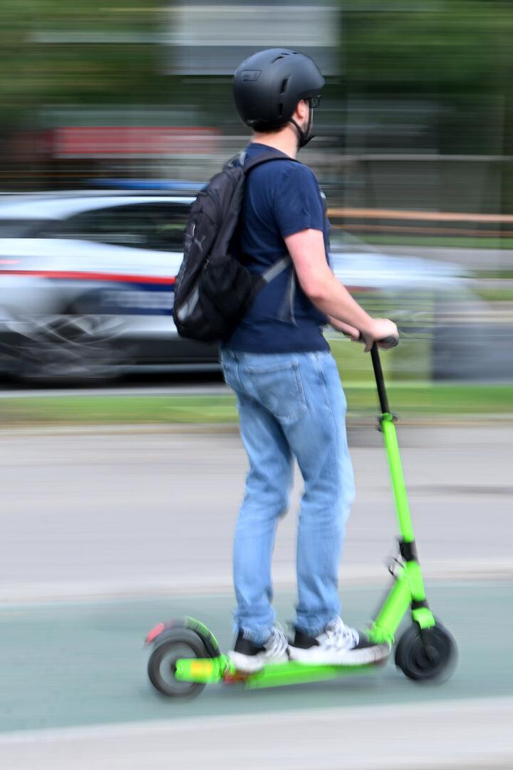 Ein Mann fährt mit einem grünen E-Scooter auf der Straße.