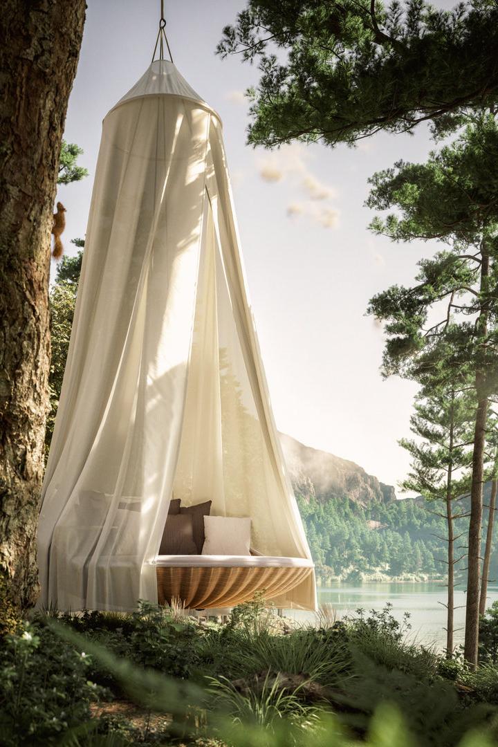 Ein hängendes Bett mit Baldachin hängt an einem Baum mit Blick auf einen See.