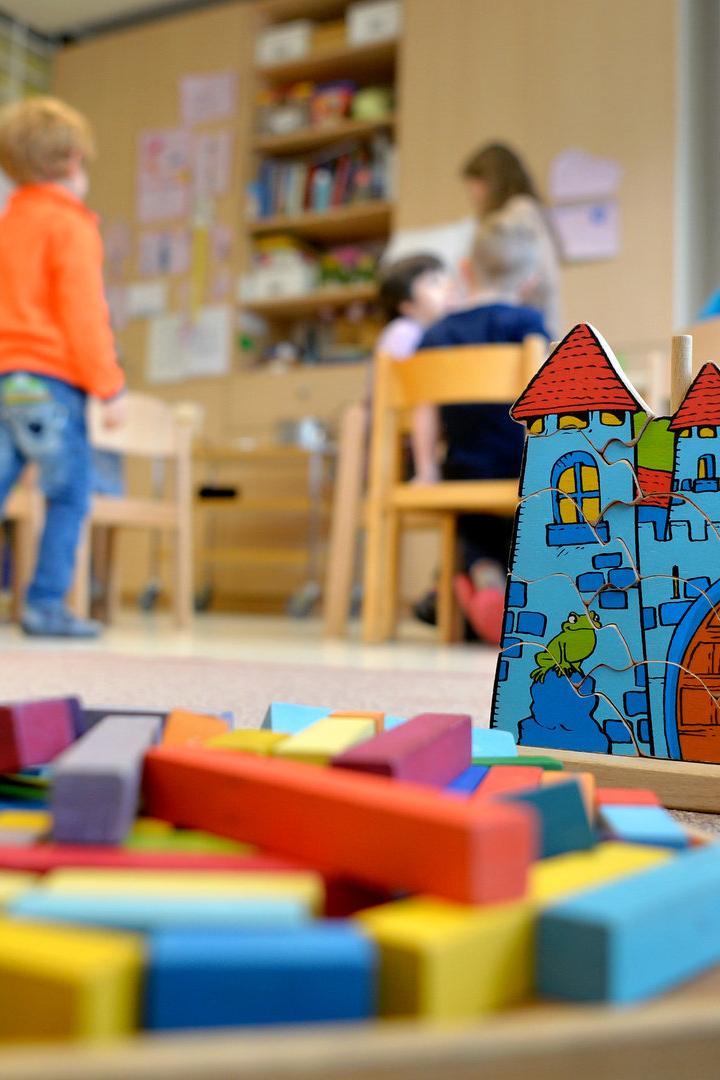 Kinder spielen mit einem Holzpuzzle und Bausteinen in einem Kindergarten.