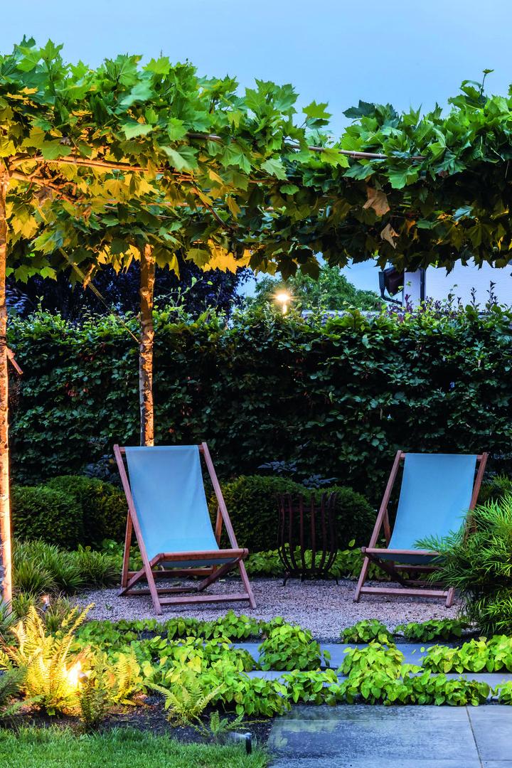 Zwei Liegestühle stehen unter Bäumen in einem gepflegten Garten.