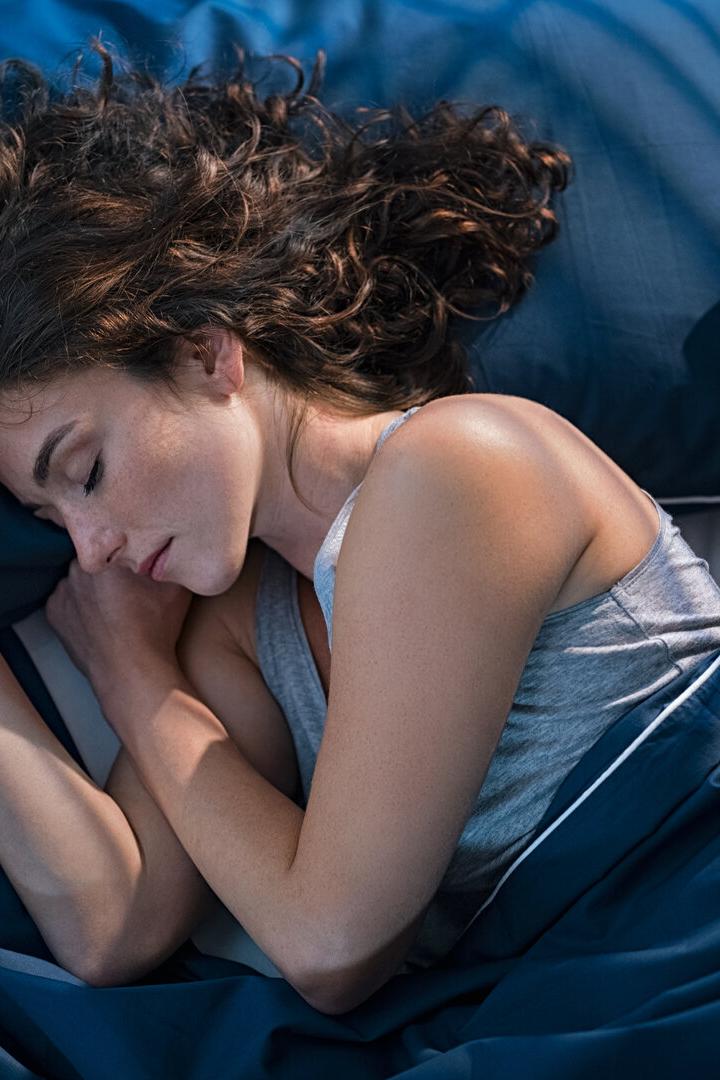 Junge Frau schläft mit Leintuch im Bett. 